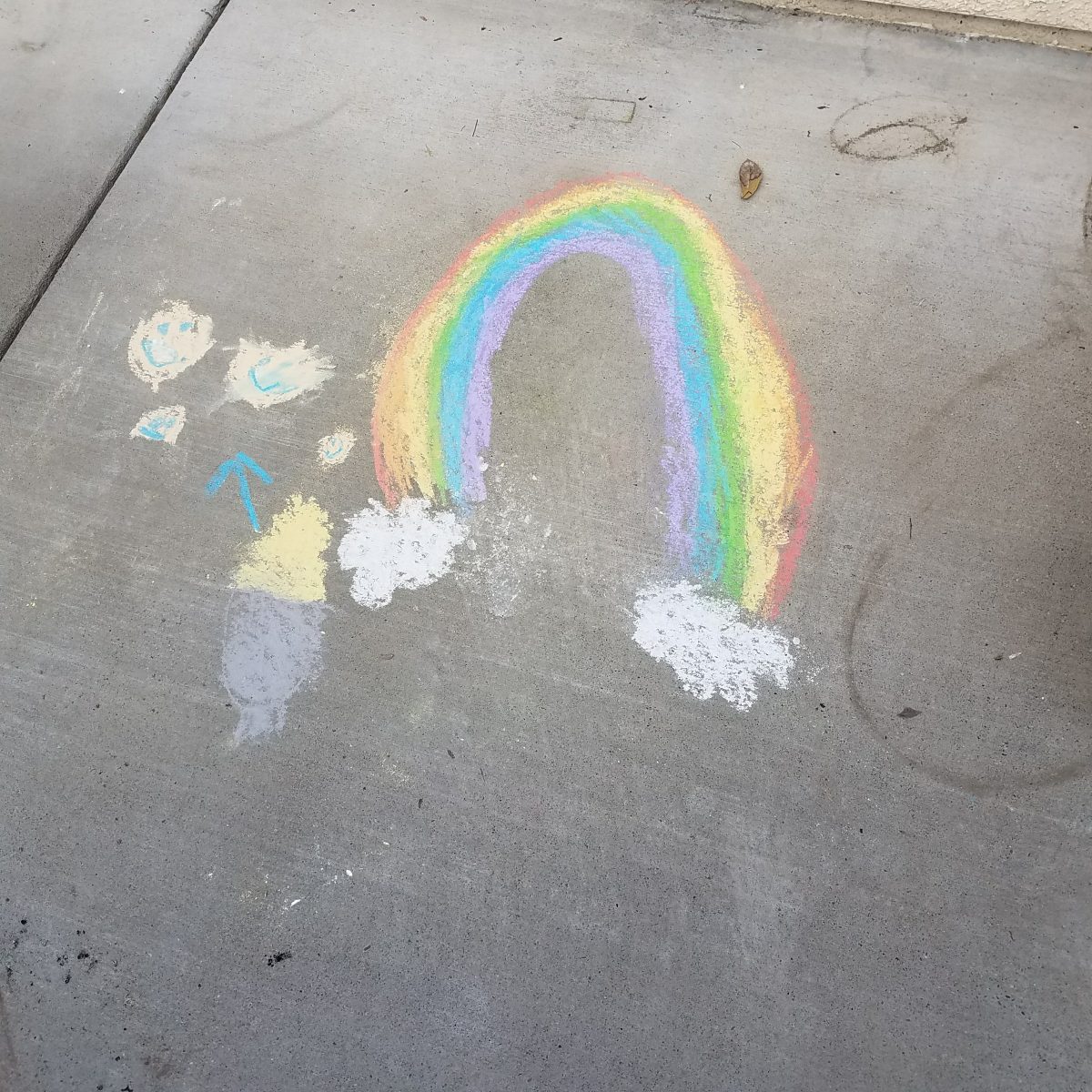 childs drawing in chalk of a rainbow on dirty sidewalk